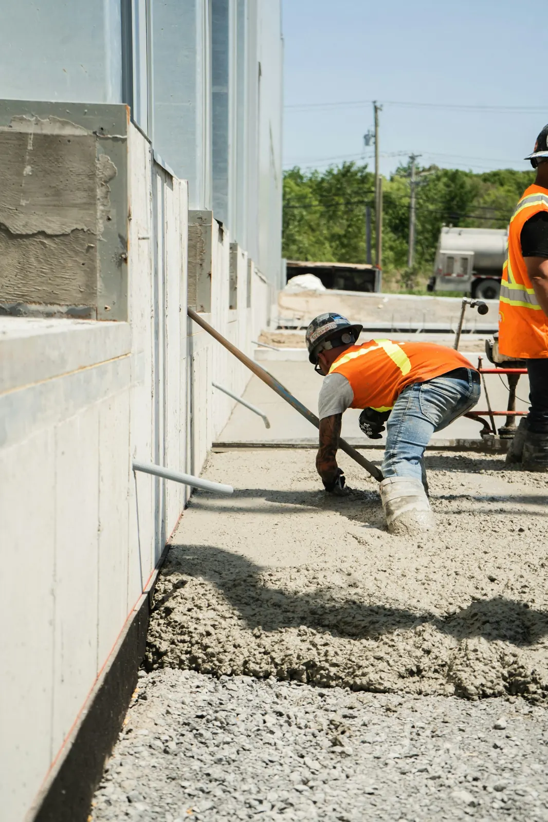 A worker in an orange vest finishing a concrete slab