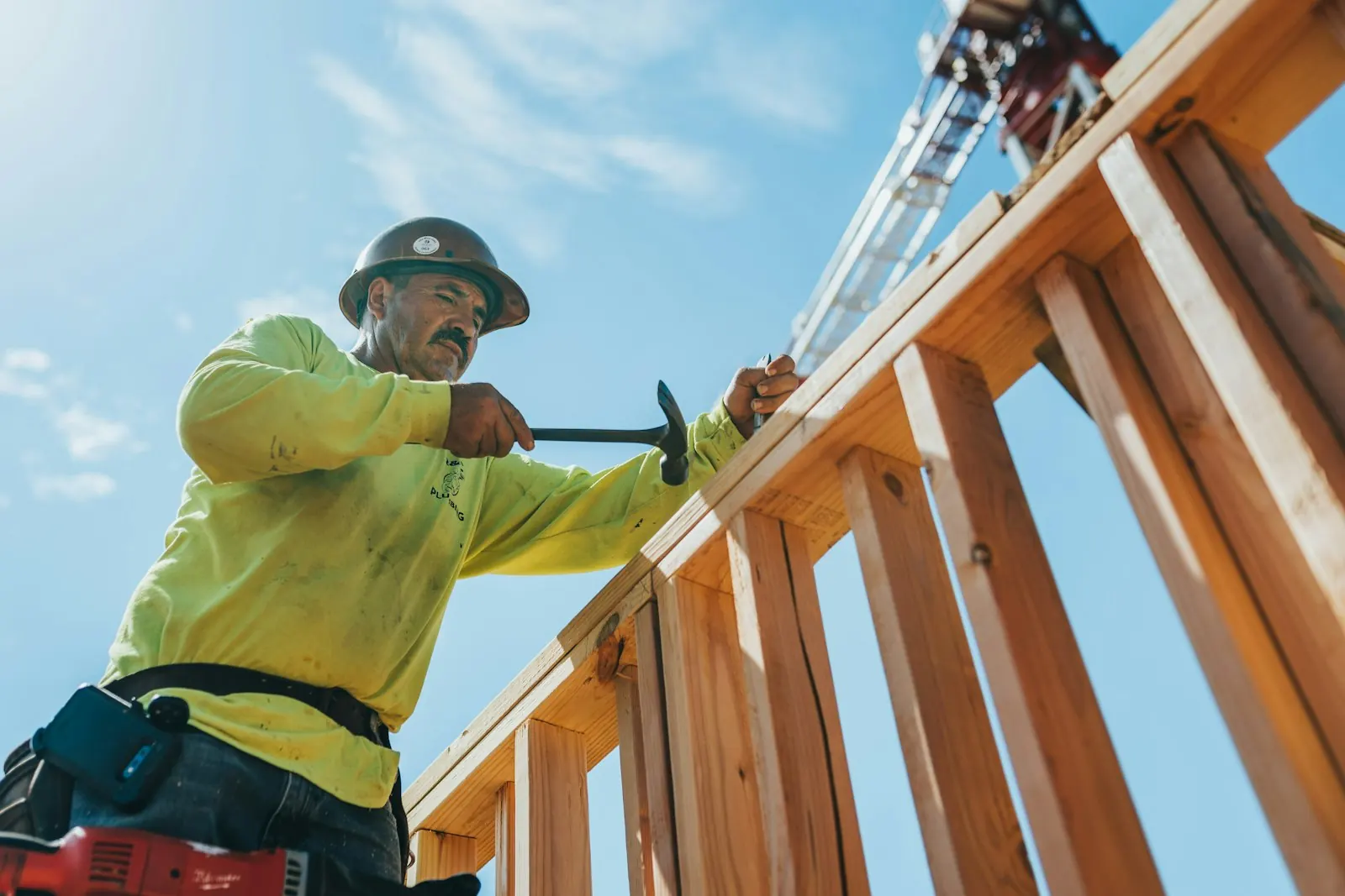 A carpenter in a hard hat hammering a wood frame