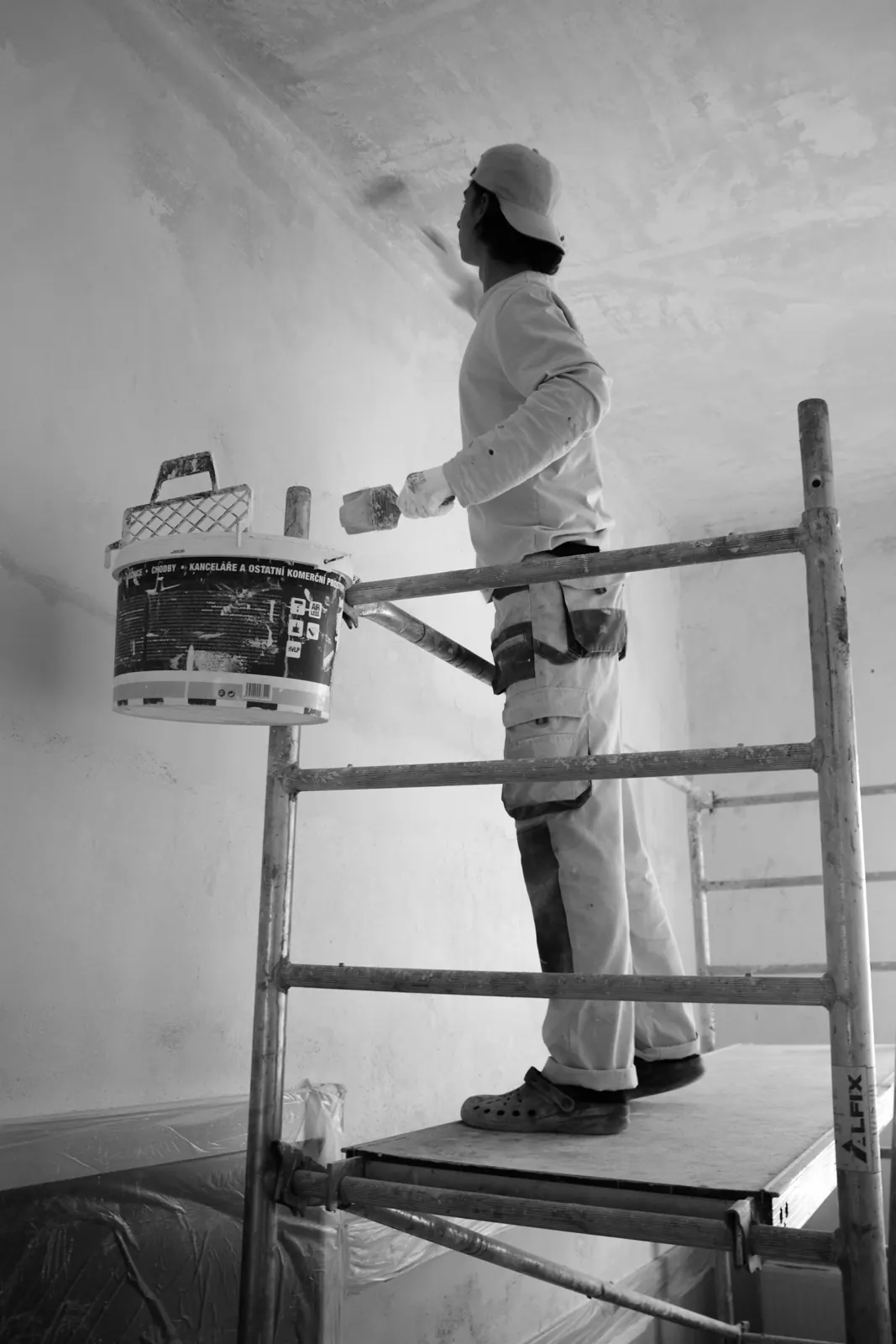 A painter rolling a wall from a scaffold platform